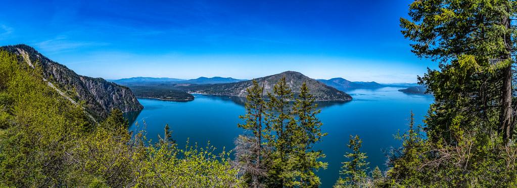 Panoramic view of a vast blue lake surrounded by green mountains under a clear sky.