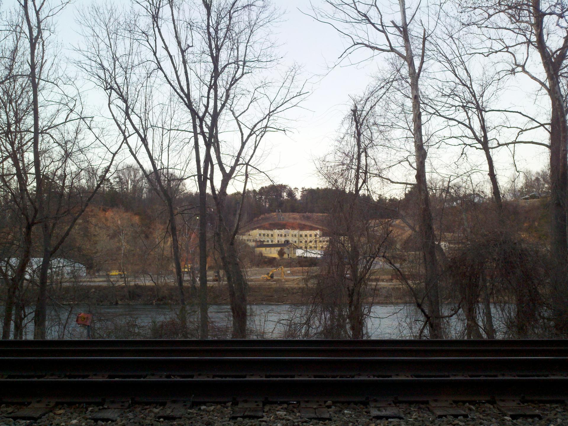 Bare trees, railroad tracks, river, and distant building under a clear sky.