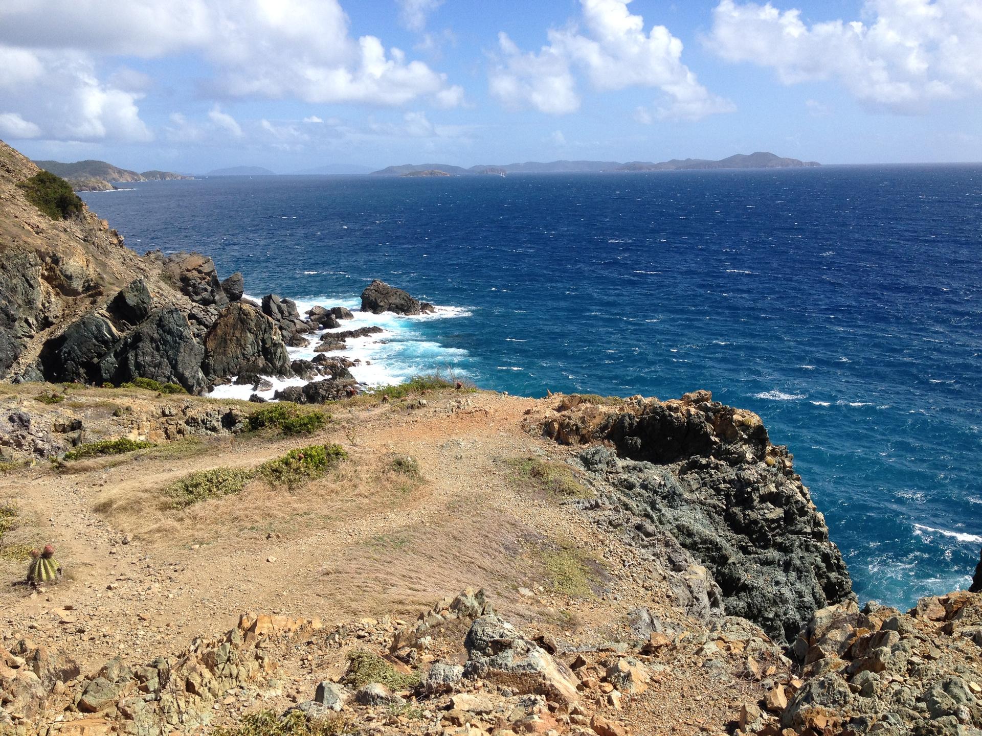 Expansive view of a rugged coastline, deep blue ocean, and distant islands.