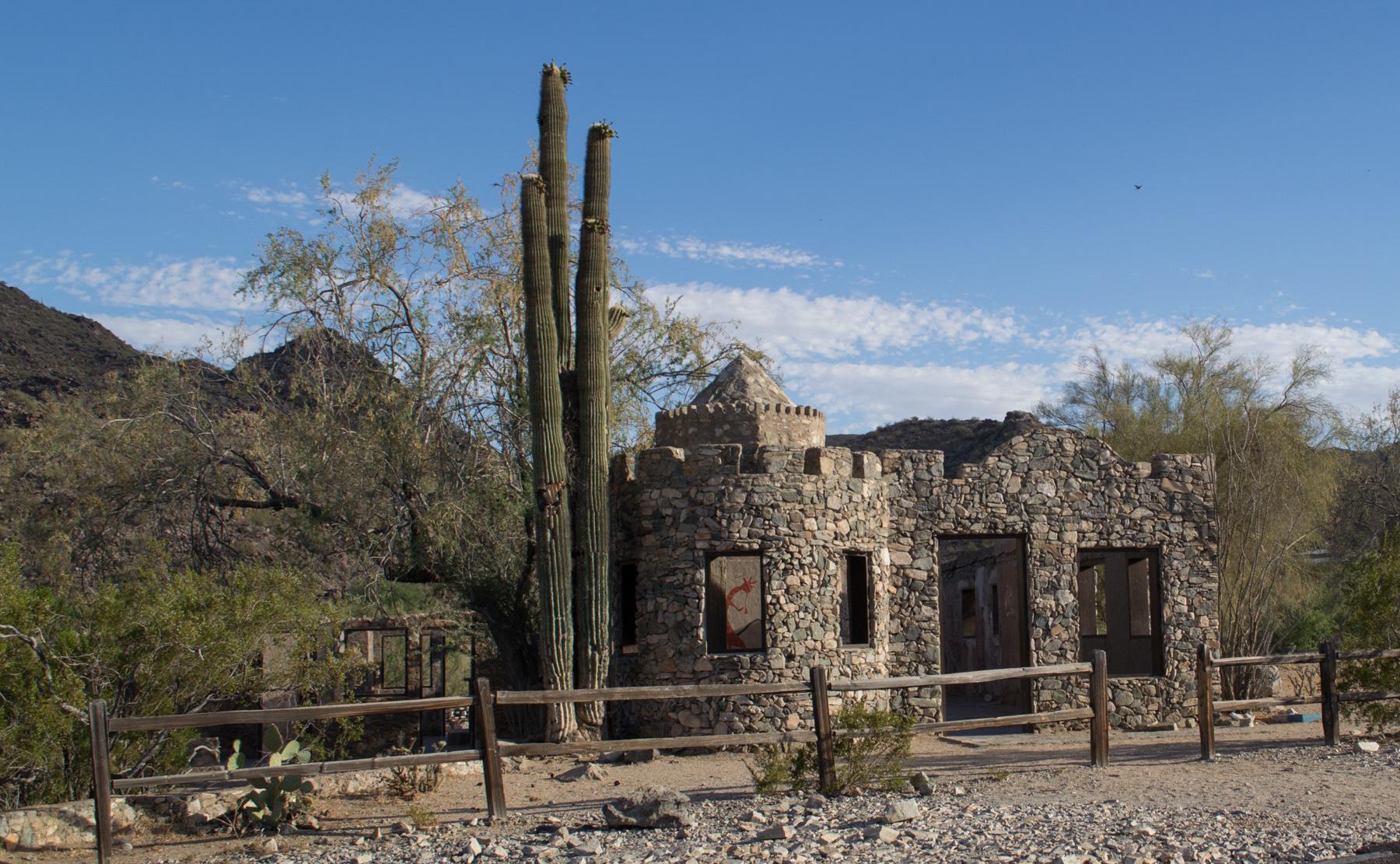 Stone castle-like building with saguaro cacti under a clear desert sky.