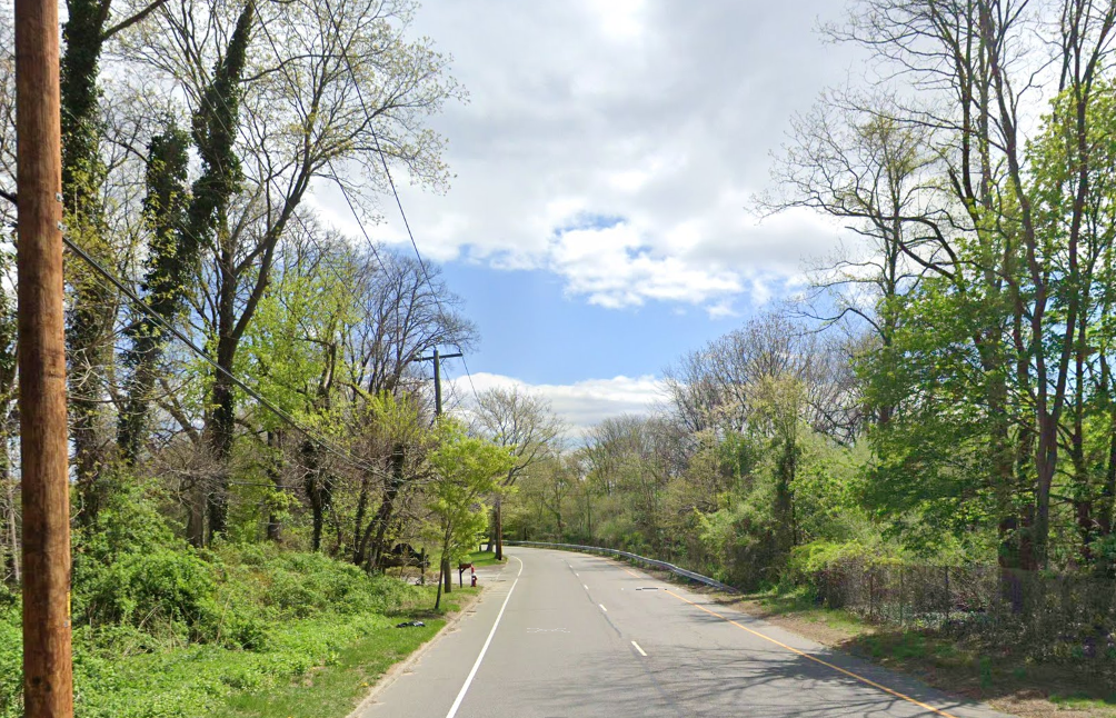 Paved road winding through dense green trees under a partly cloudy sky.