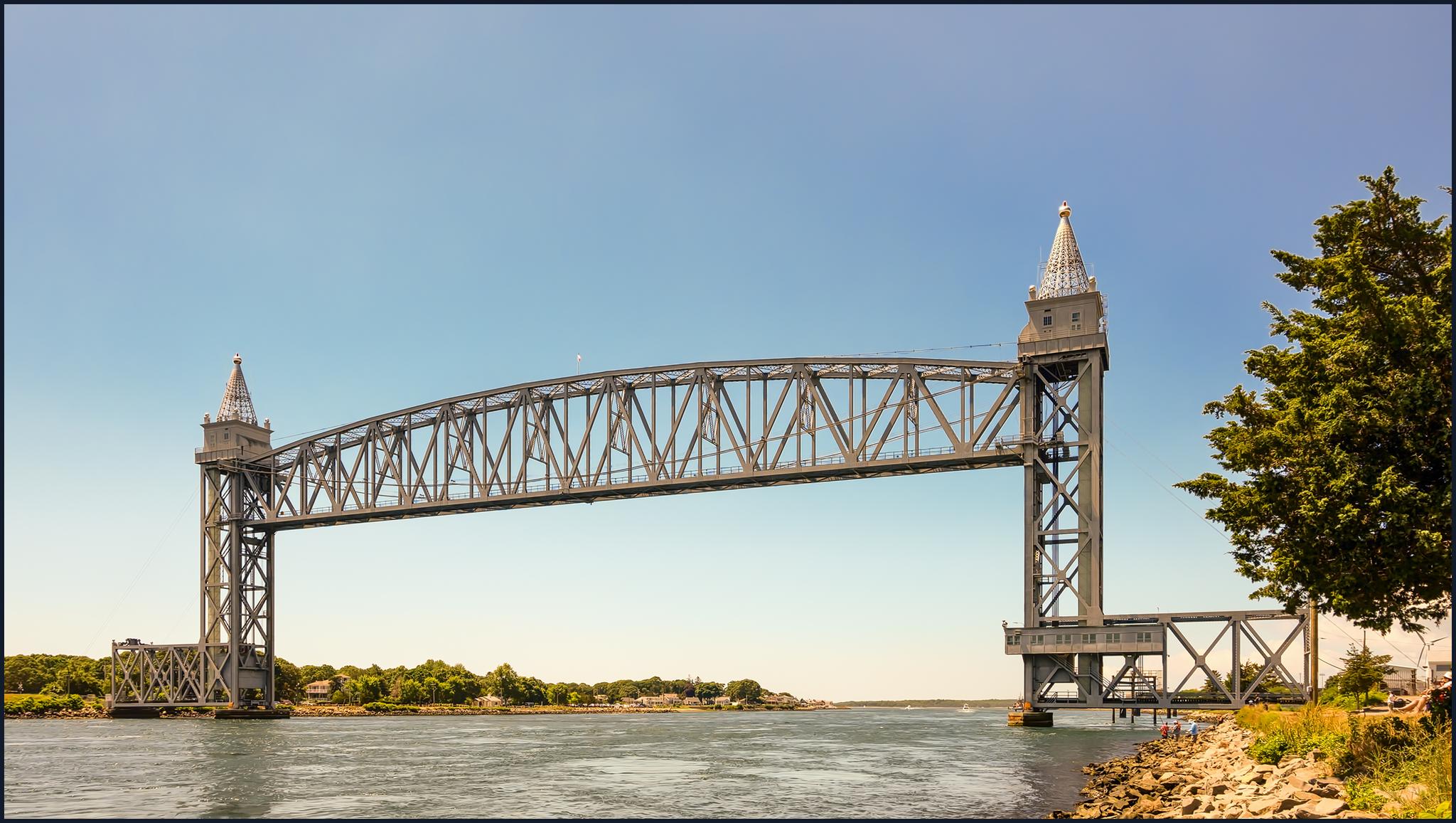 Large steel truss bridge spans calm water under a clear blue sky.