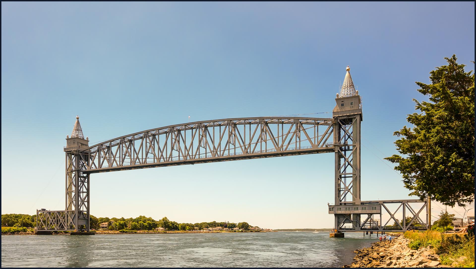Large steel truss bridge spans calm water under a clear blue sky.
