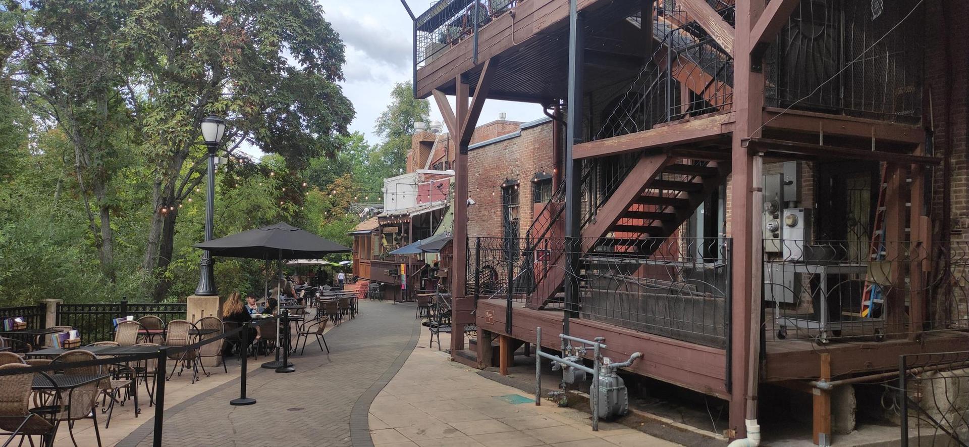 Outdoor patio seating with people next to a multi-story wooden building.