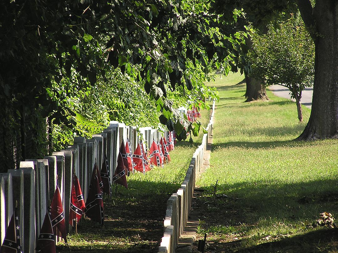 Row of grave markers with small flags in a sunny, grassy area with trees. - Campaign Ride