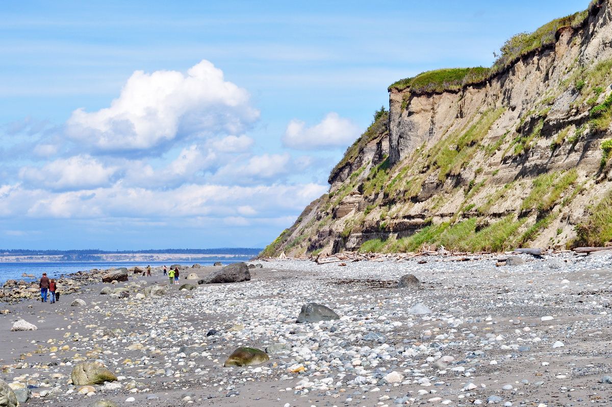Sunny day on a rocky beach with people walking near a tall, green cliff. - North Beach to Glass Beach