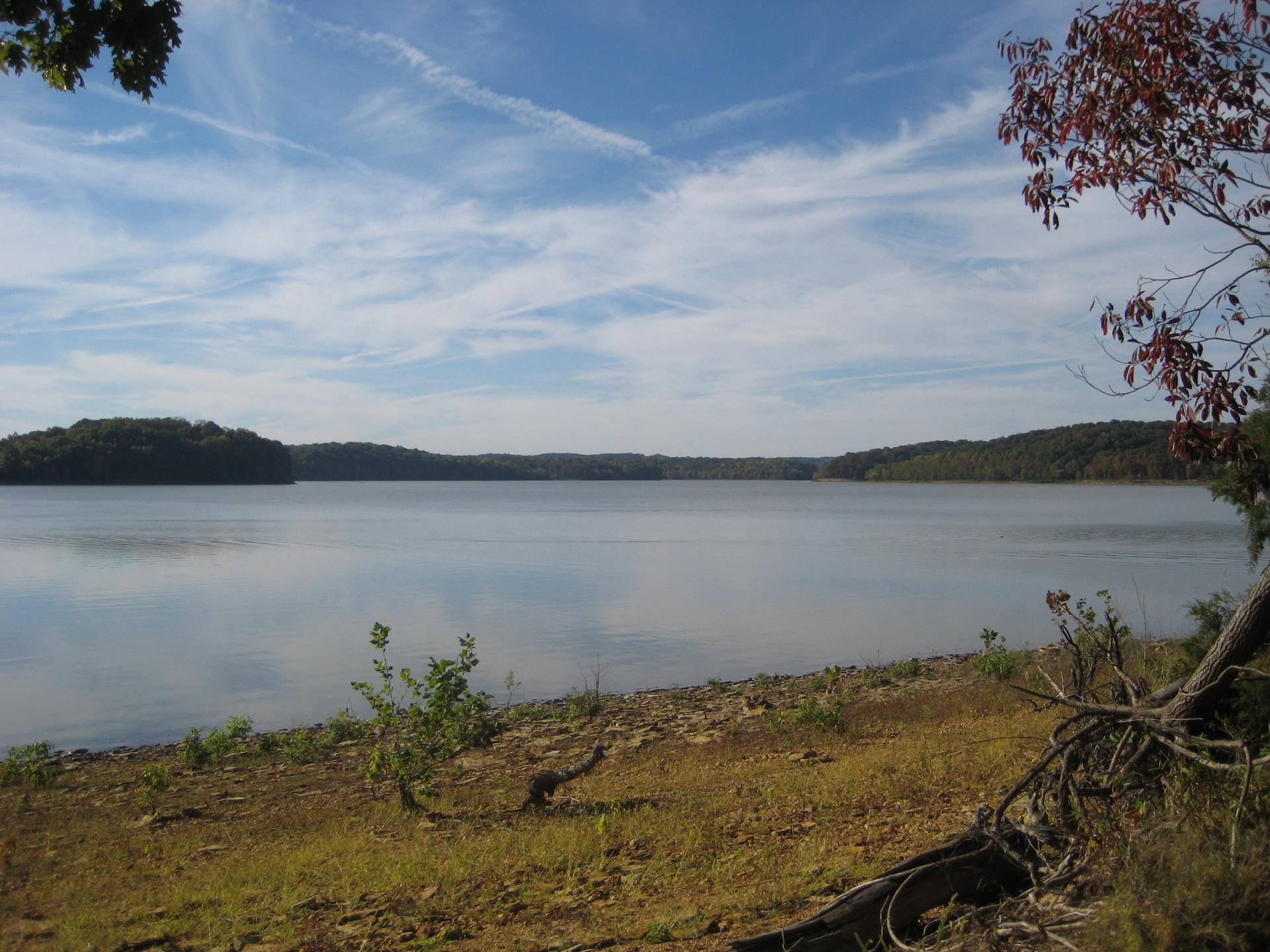Wide lake under a partly cloudy sky, surrounded by distant forested hills.