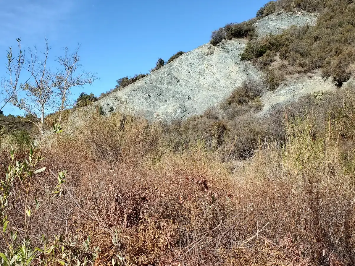 A steep, rocky hillside covered in dry brush under a clear sky.