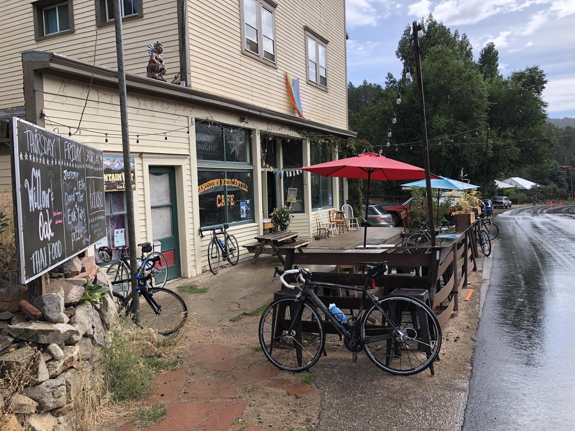 Cafe exterior with outdoor seating and parked bicycles on a wet, overcast day.