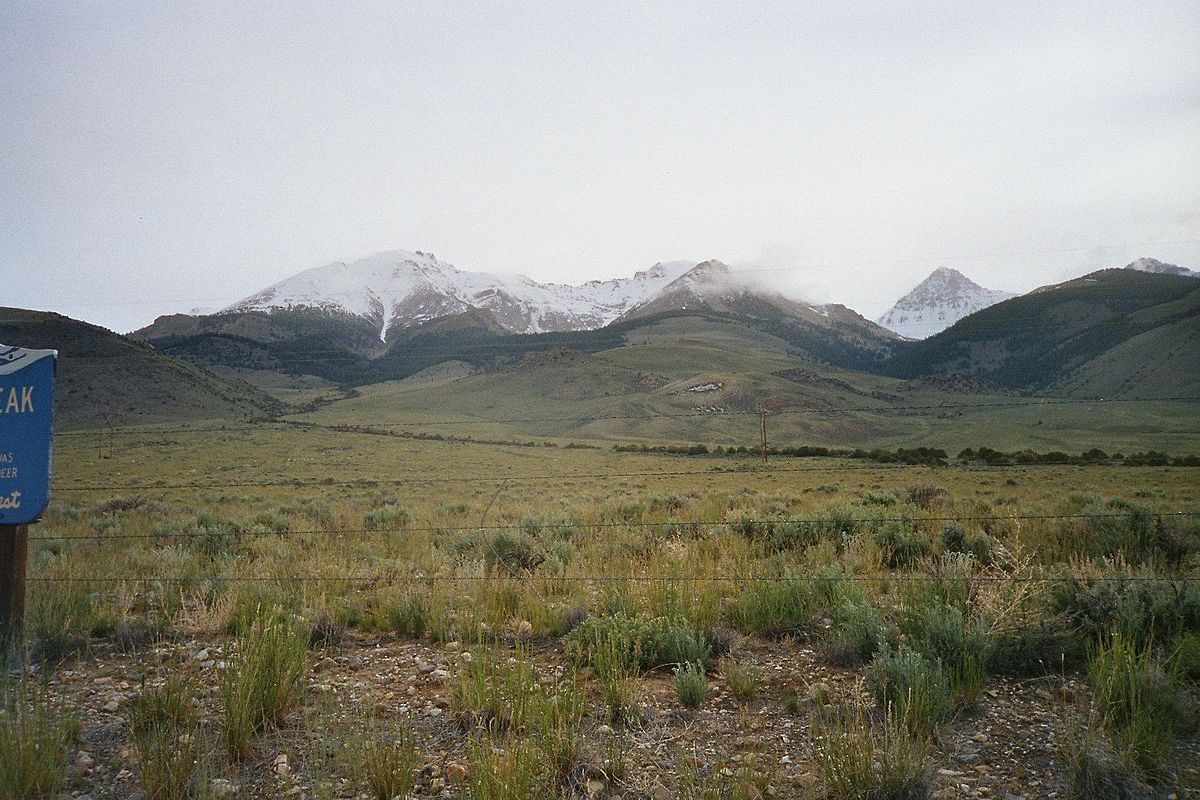 Overcast view of snow-capped mountains behind a vast, grassy field. - Leatherman Peak Loop from Sawmill Gulch Road