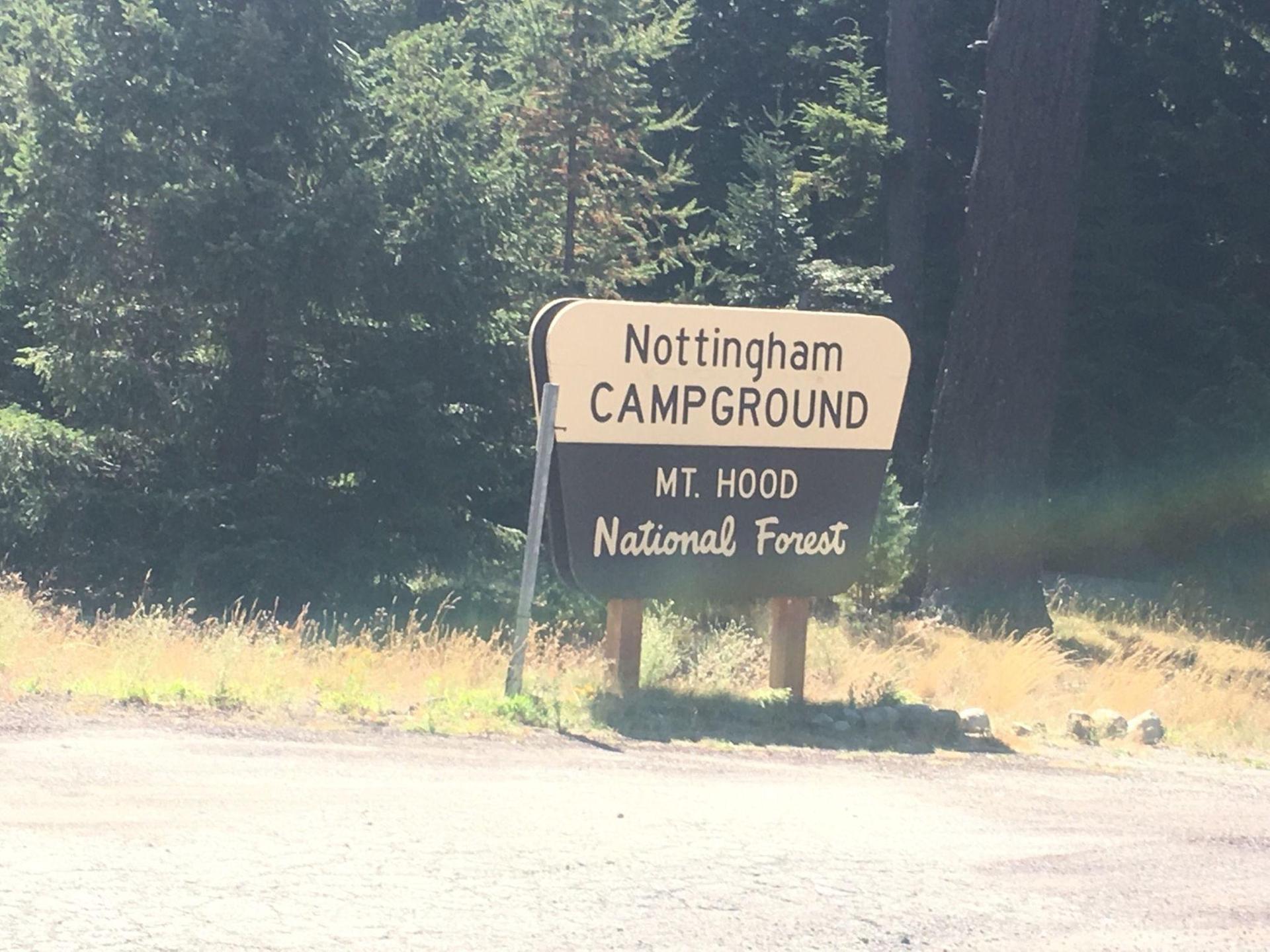 A brown and white sign stands by a dirt road near trees.