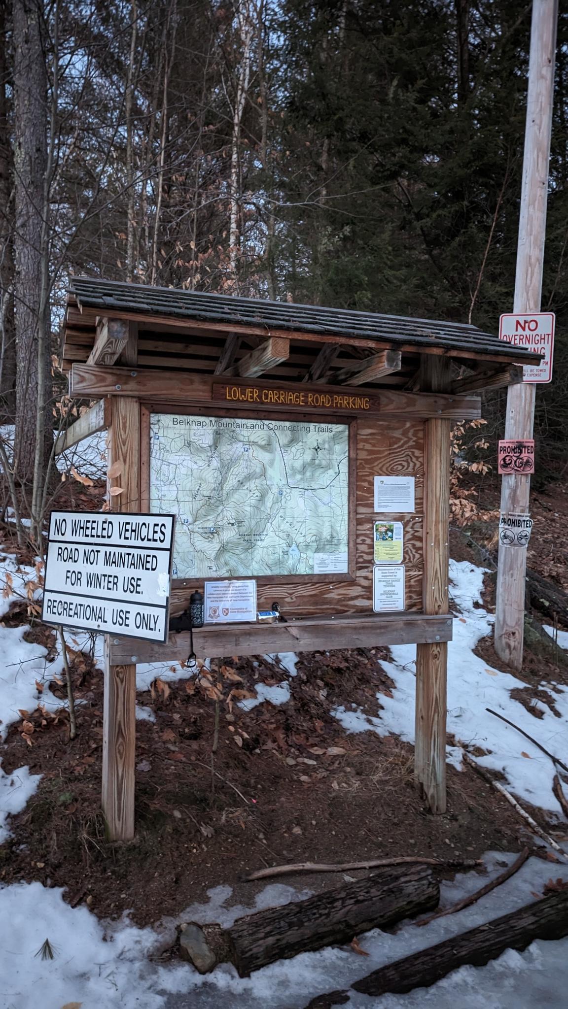 Wooden information kiosk with map in snowy woods on a clear day.