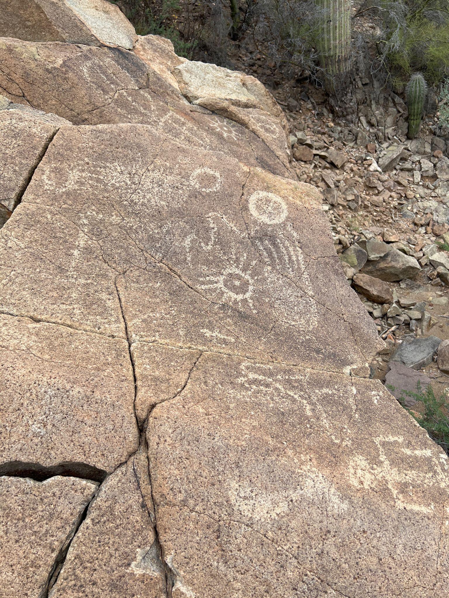 Petroglyphs on a large sunlit rock in a dry, rocky environment.