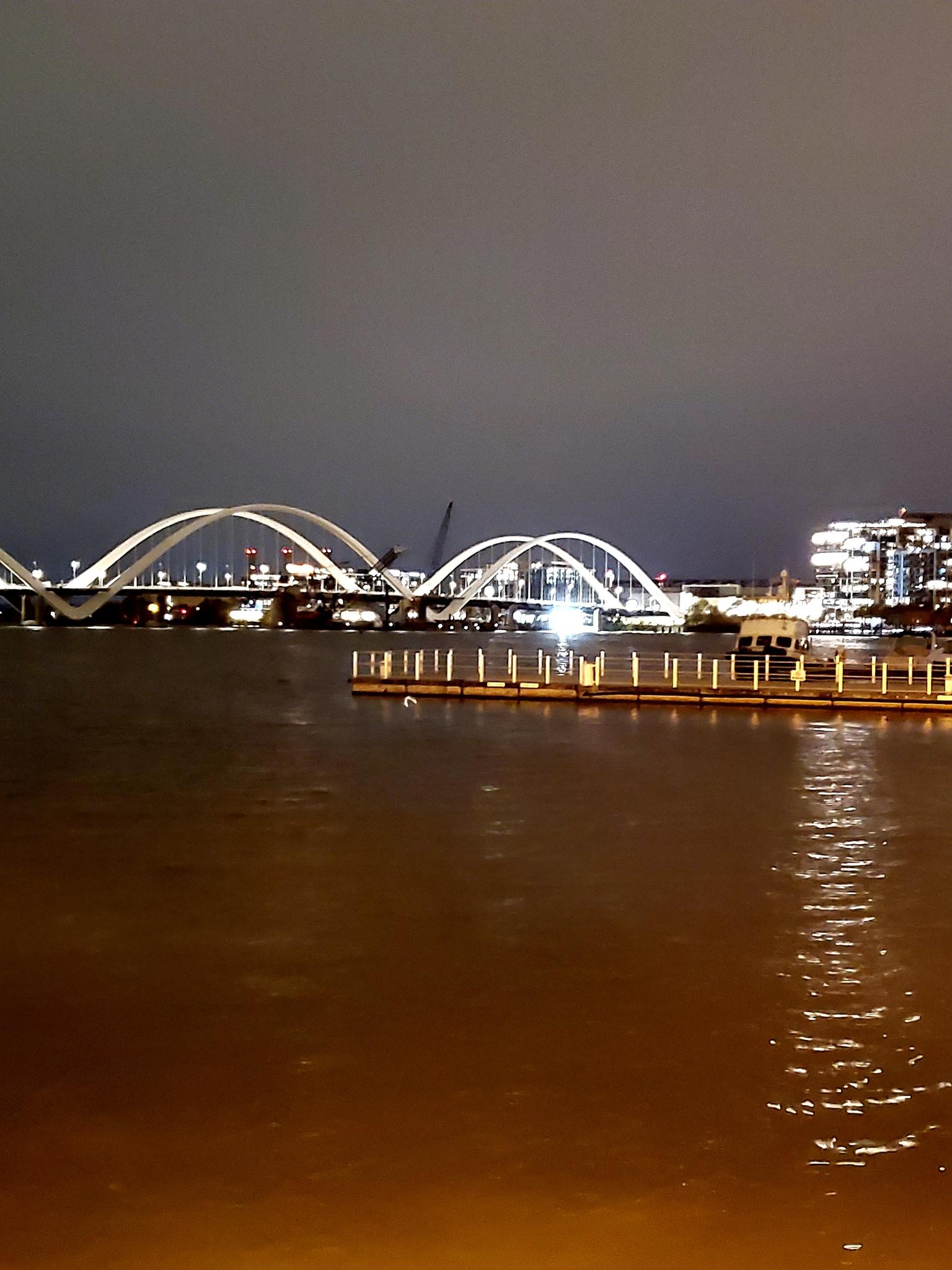 Two illuminated arch bridges span dark water at night with city lights.