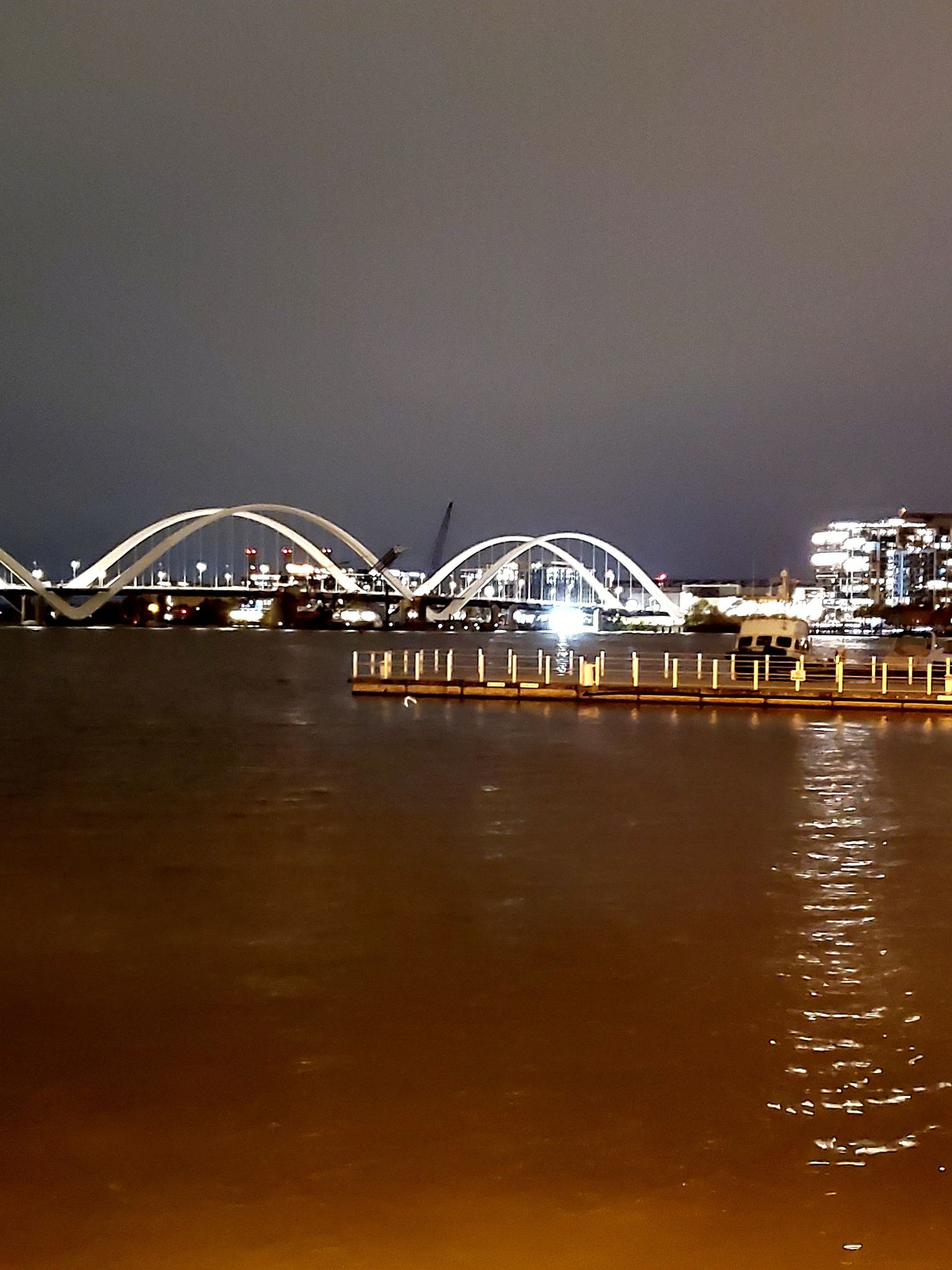 Two illuminated arch bridges span dark water at night with city lights. - Canal Basin at Navy Yard – Navy Yard Boardwalk loop from United States House of Representatives