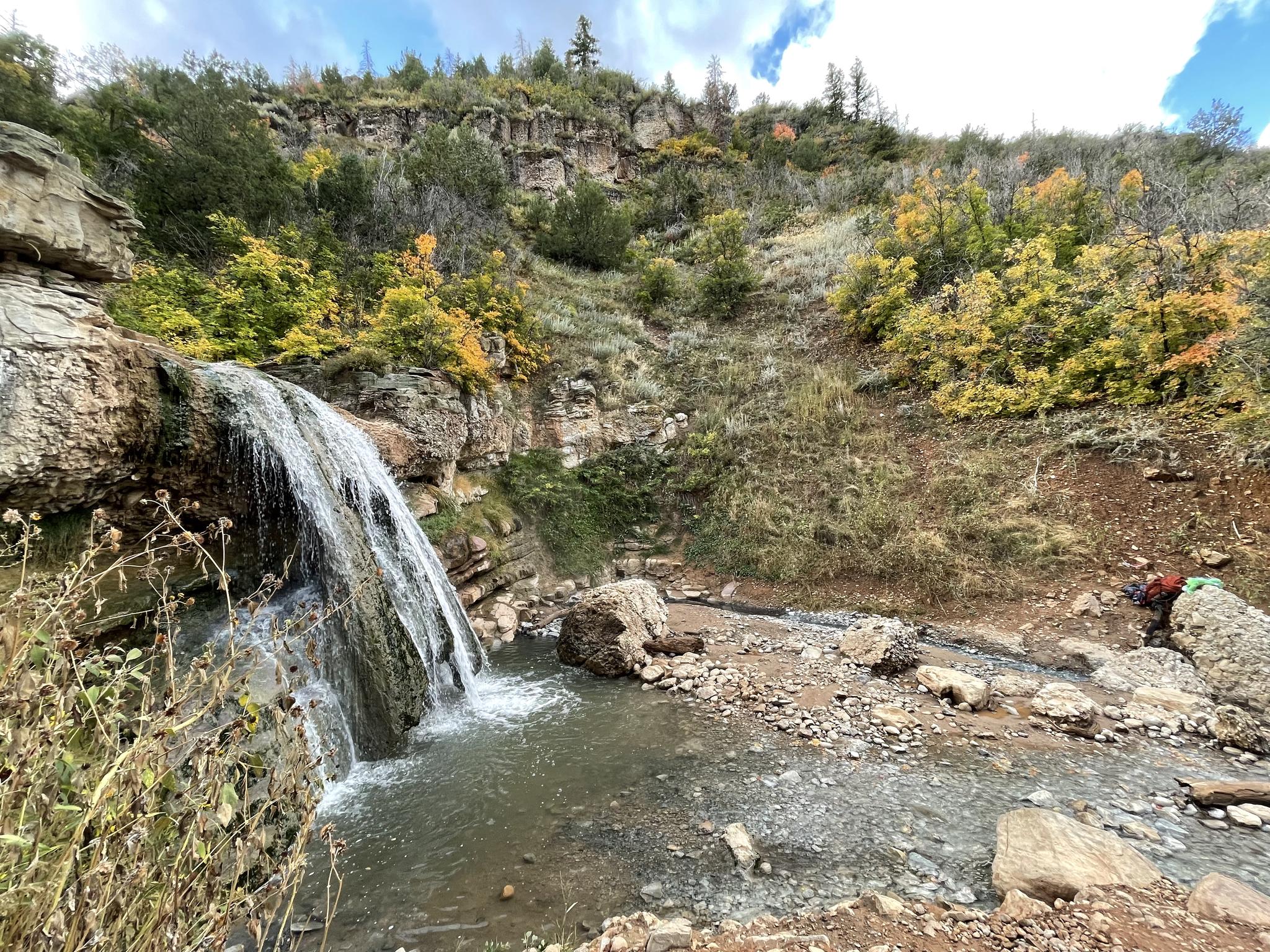 Waterfall flowing into a stream, surrounded by colorful autumn trees, with one person.