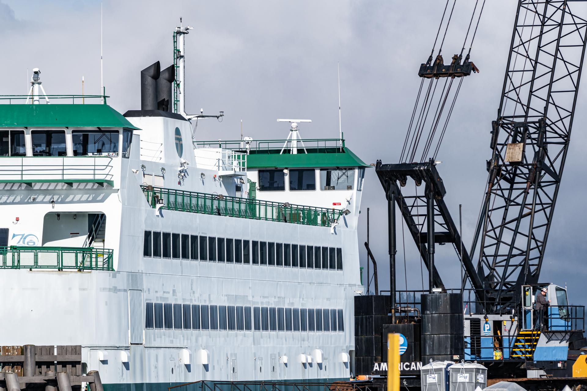Large white and green ferry docked next to a tall industrial crane.