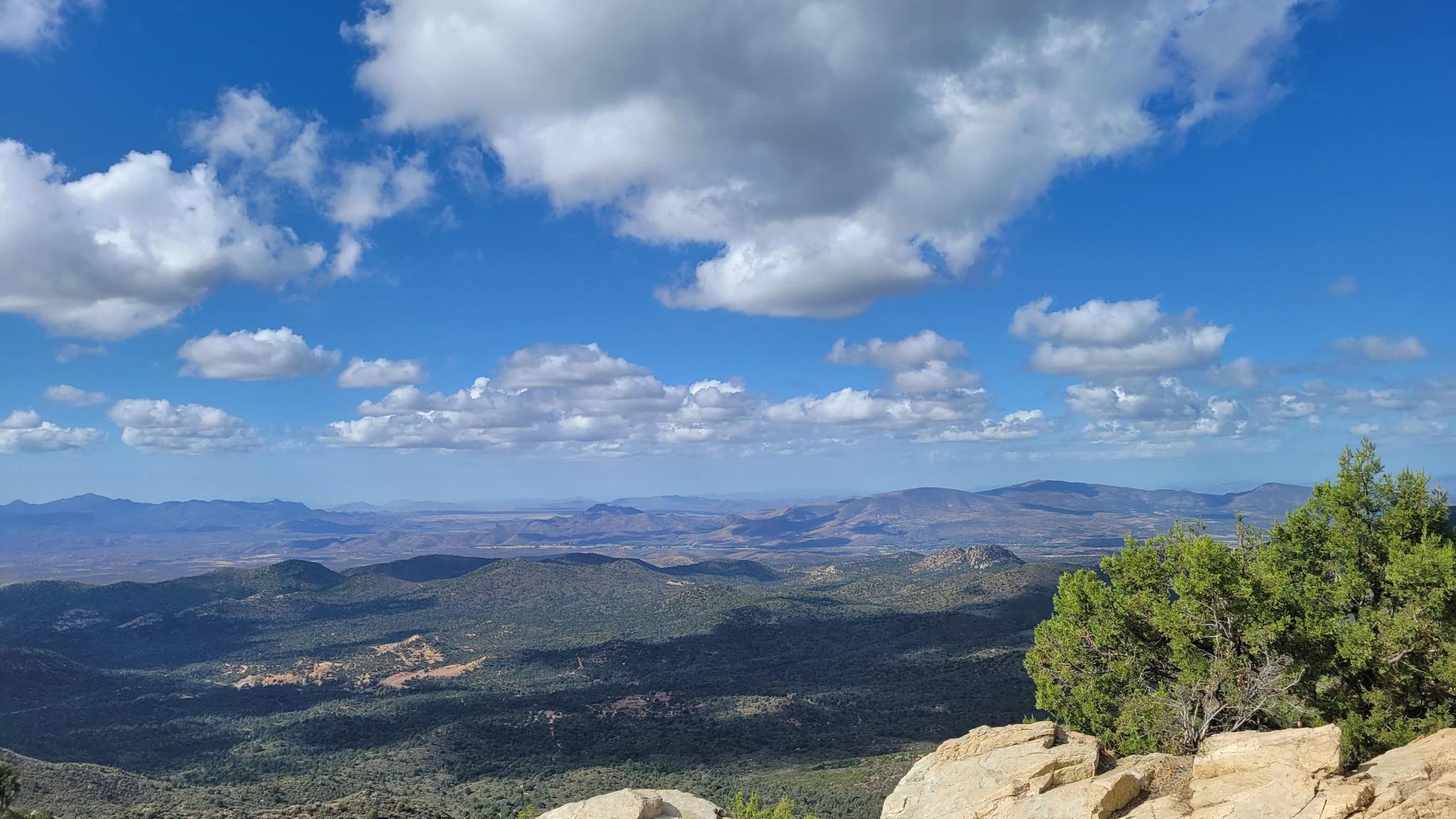 Expansive mountain vista under a bright blue sky with fluffy white clouds.