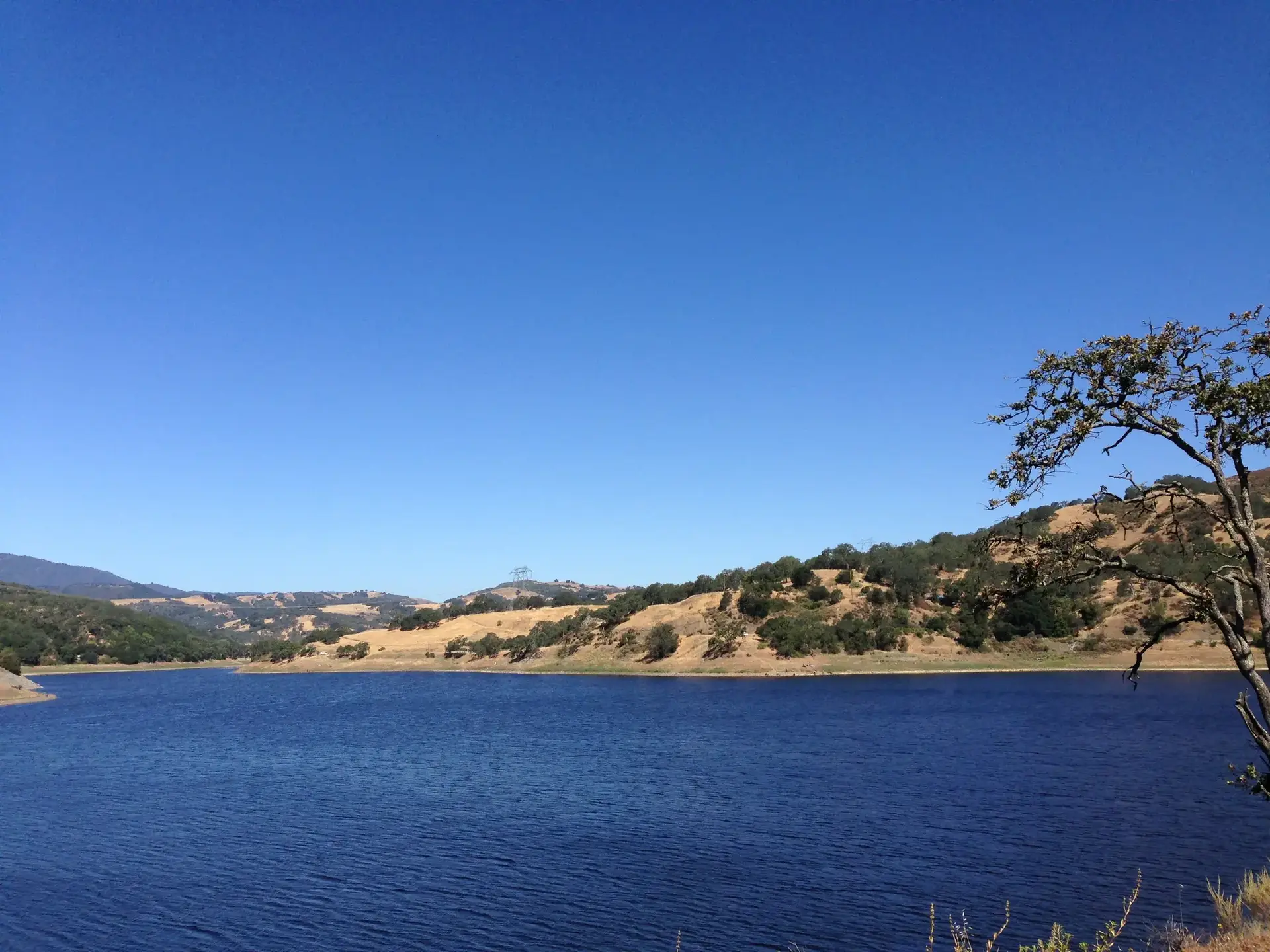 Deep blue lake bordered by dry golden hills under a clear sky.