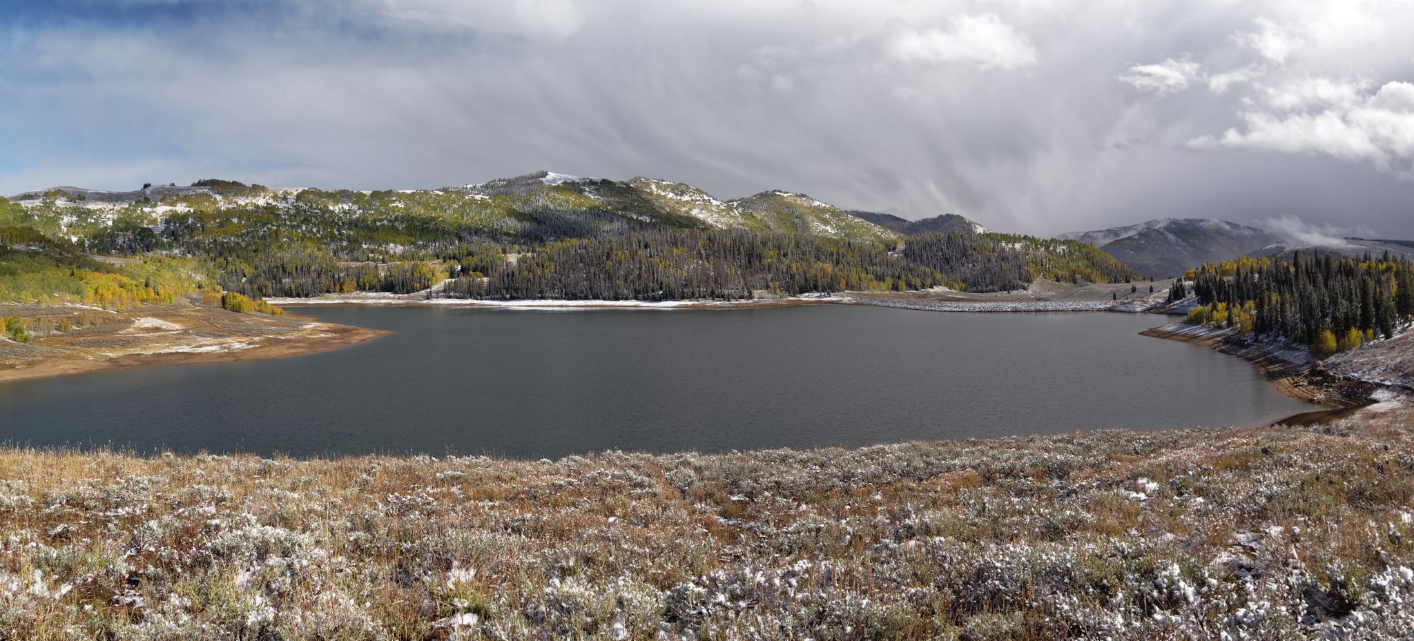 Panoramic view of a large lake surrounded by snow-dusted mountains and forests. - Left Fork of Huntington Canyon National Recreation Trail