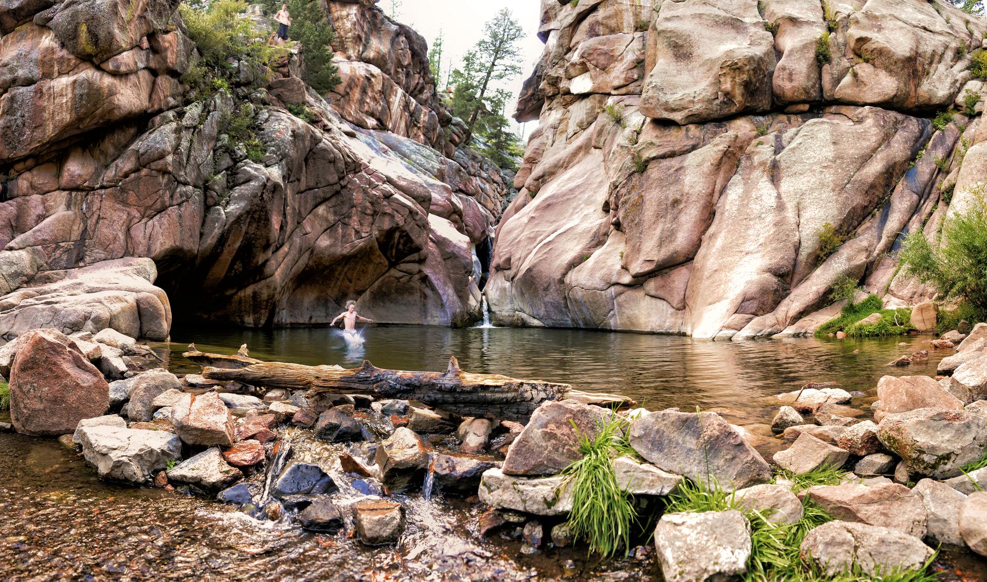 Swimmer in a natural pool, surrounded by towering rock cliffs under bright light.