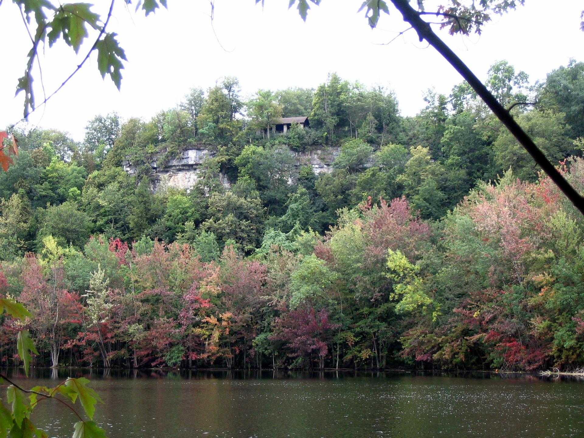 Overcast view of a lake, autumn trees, and a building on a rocky cliff.