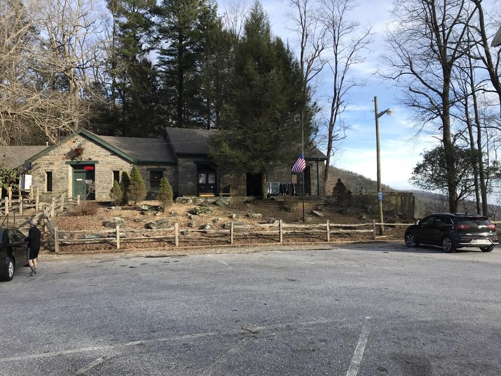 Stone building with cars in a parking lot, surrounded by trees, under bright sky.