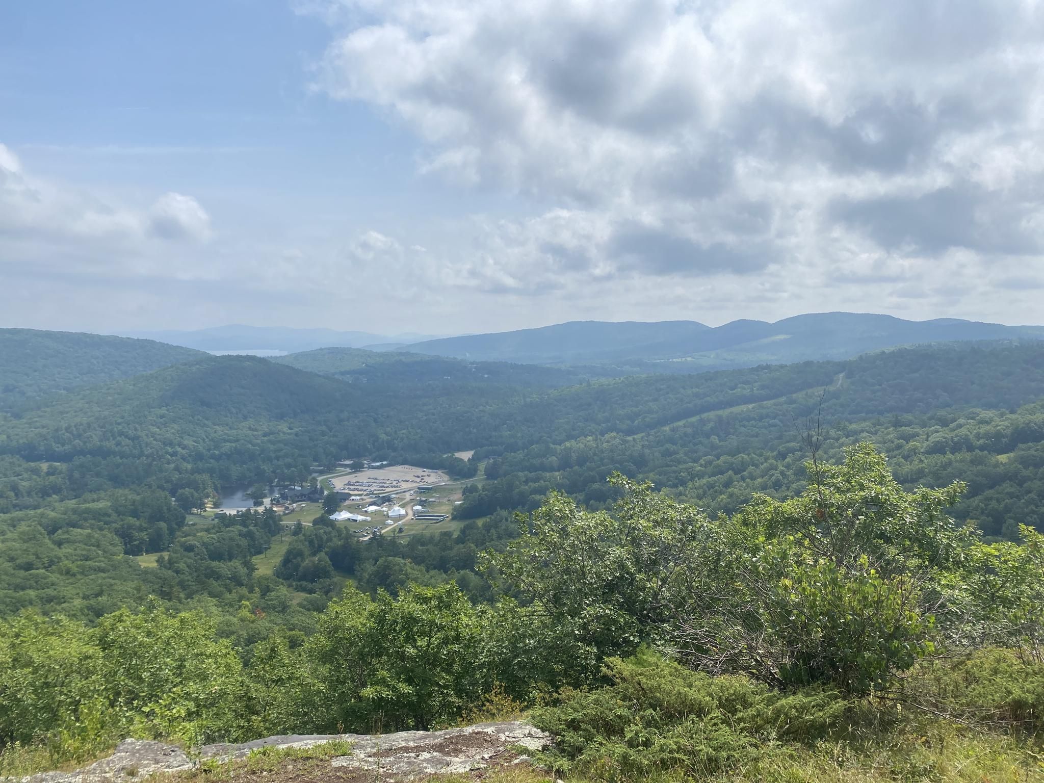 Expansive view of green forested mountains and a valley under a partly cloudy sky. - Mt. Rowe Trail