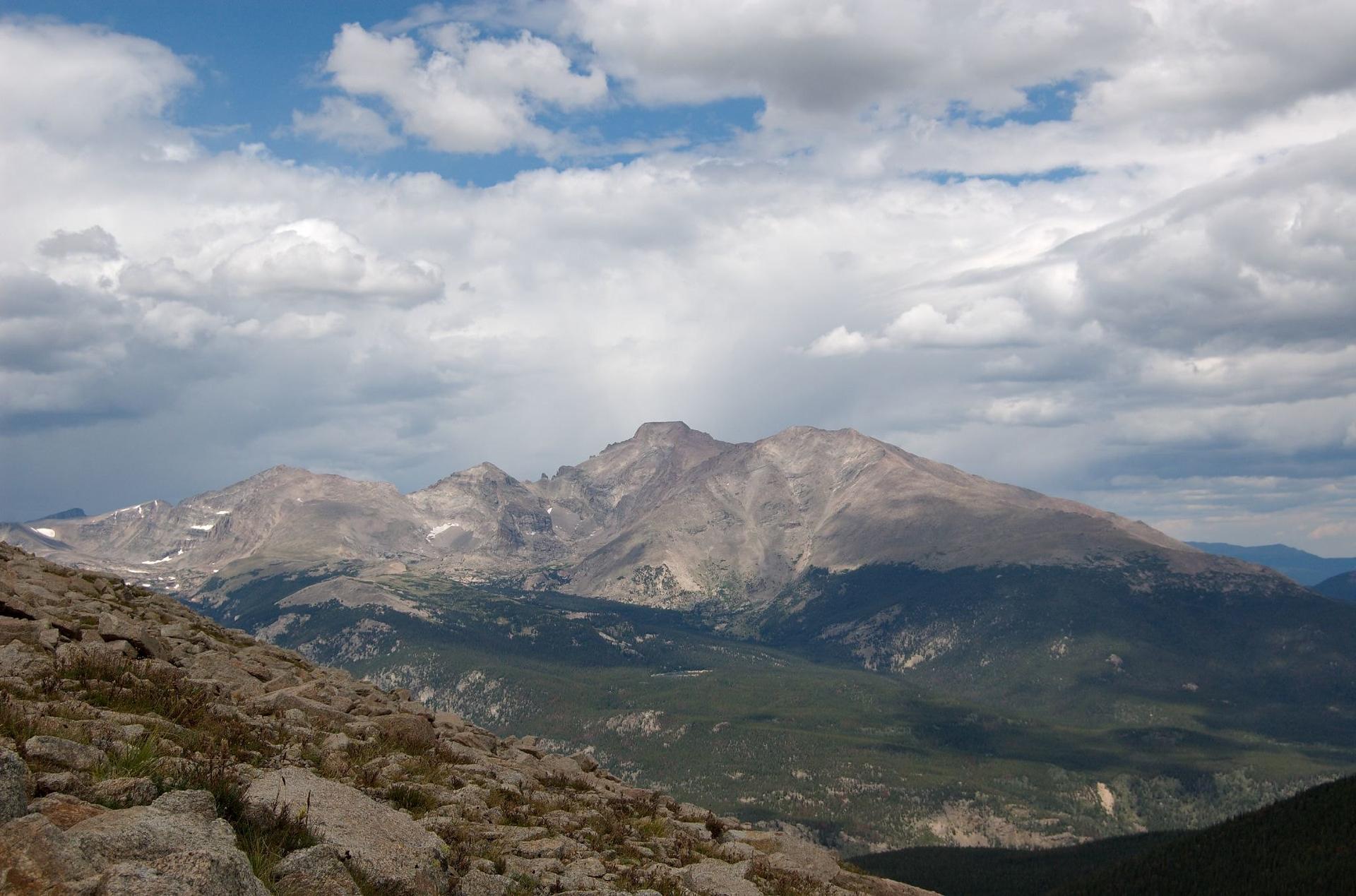 A rugged, rocky foreground overlooks distant mountains under a dramatic cloudy sky.