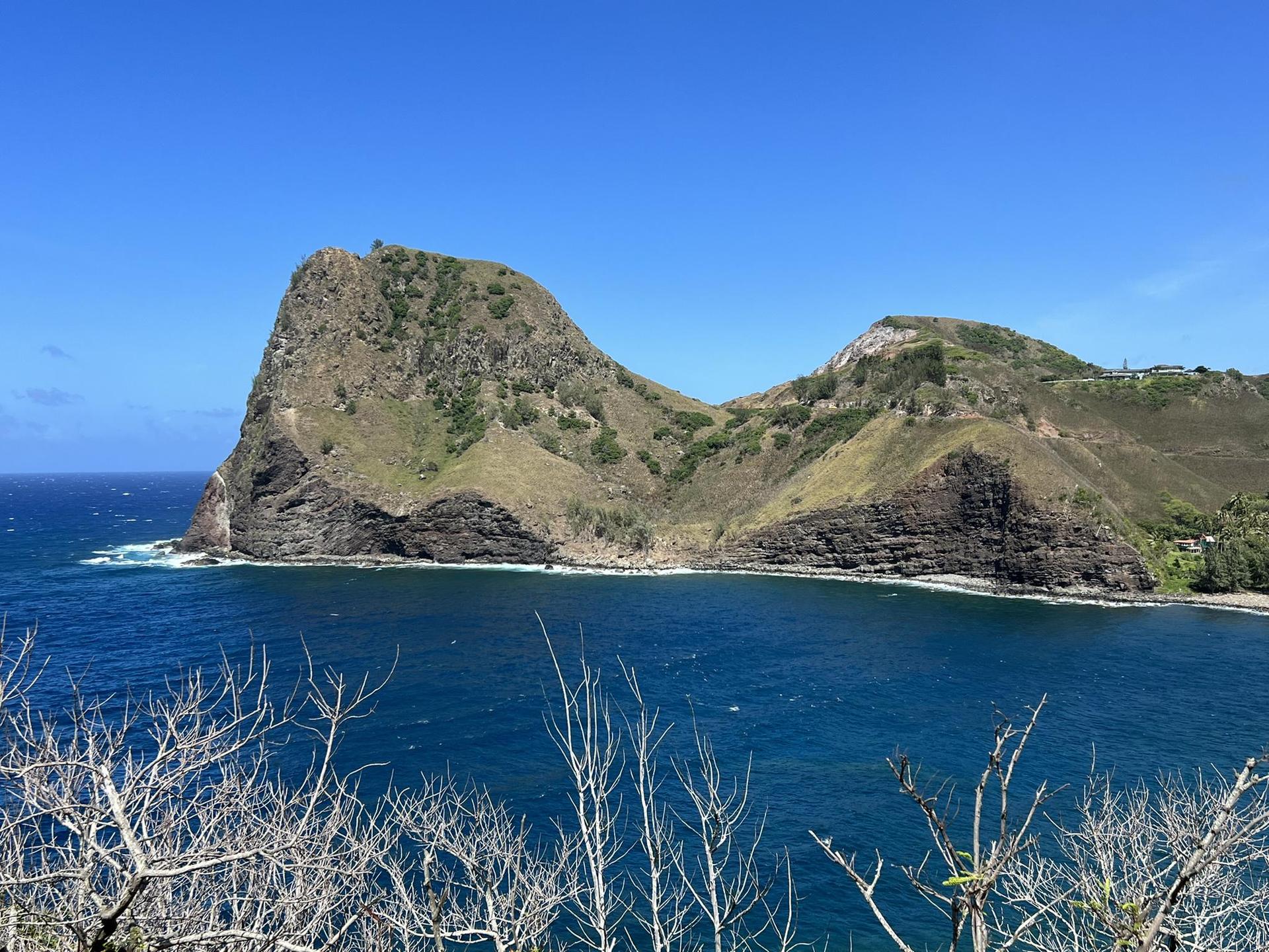Sunny coastal view of a bay with blue water and green, rocky mountains.
