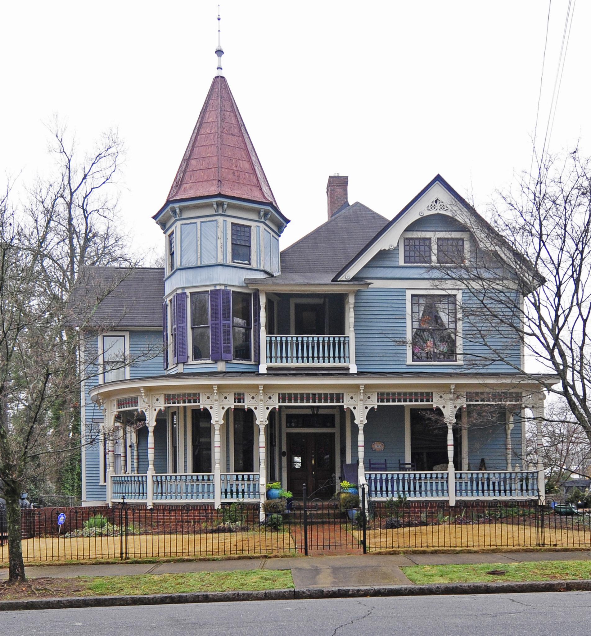 Ornate blue Victorian house with a red turret roof under an overcast sky.
