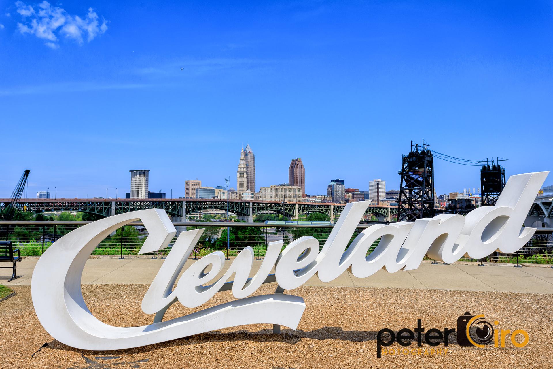 Large white sign in foreground with a city skyline and bridge under blue sky.
