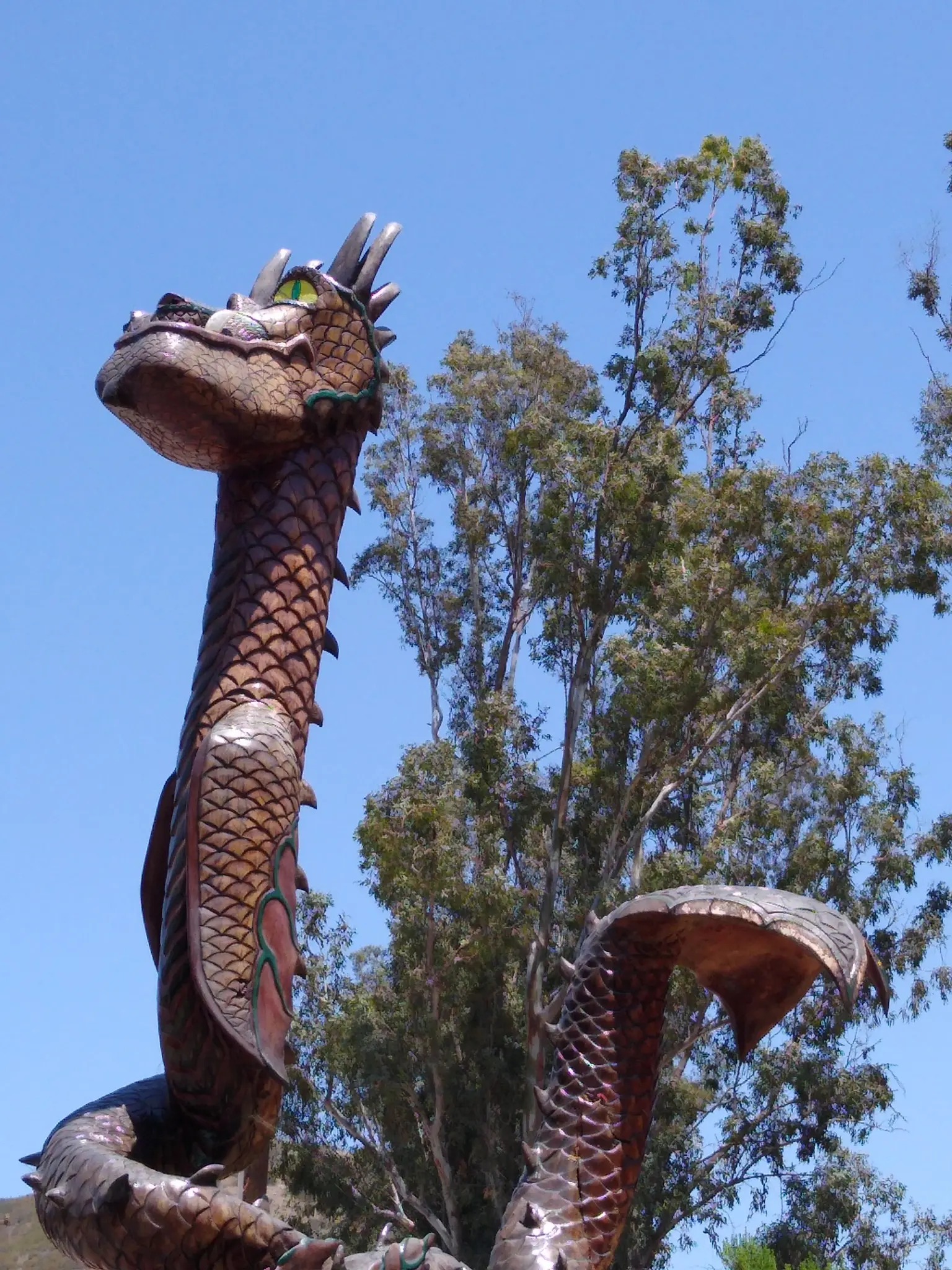 Close-up of a detailed dragon sculpture with green eyes under a bright blue sky.