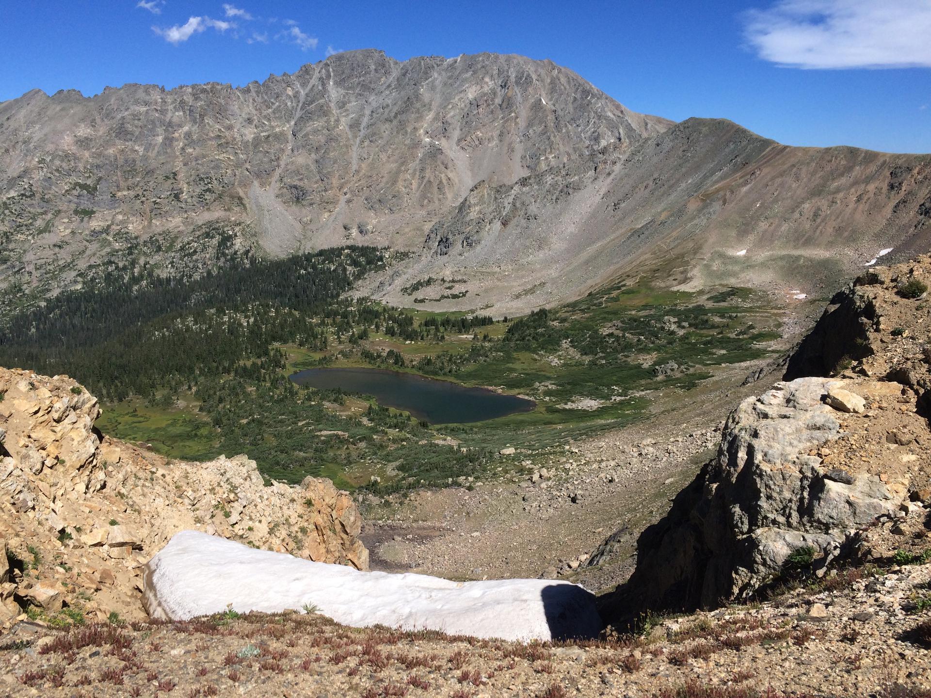 A high-angle view of a mountain lake nestled in a green valley below peaks.