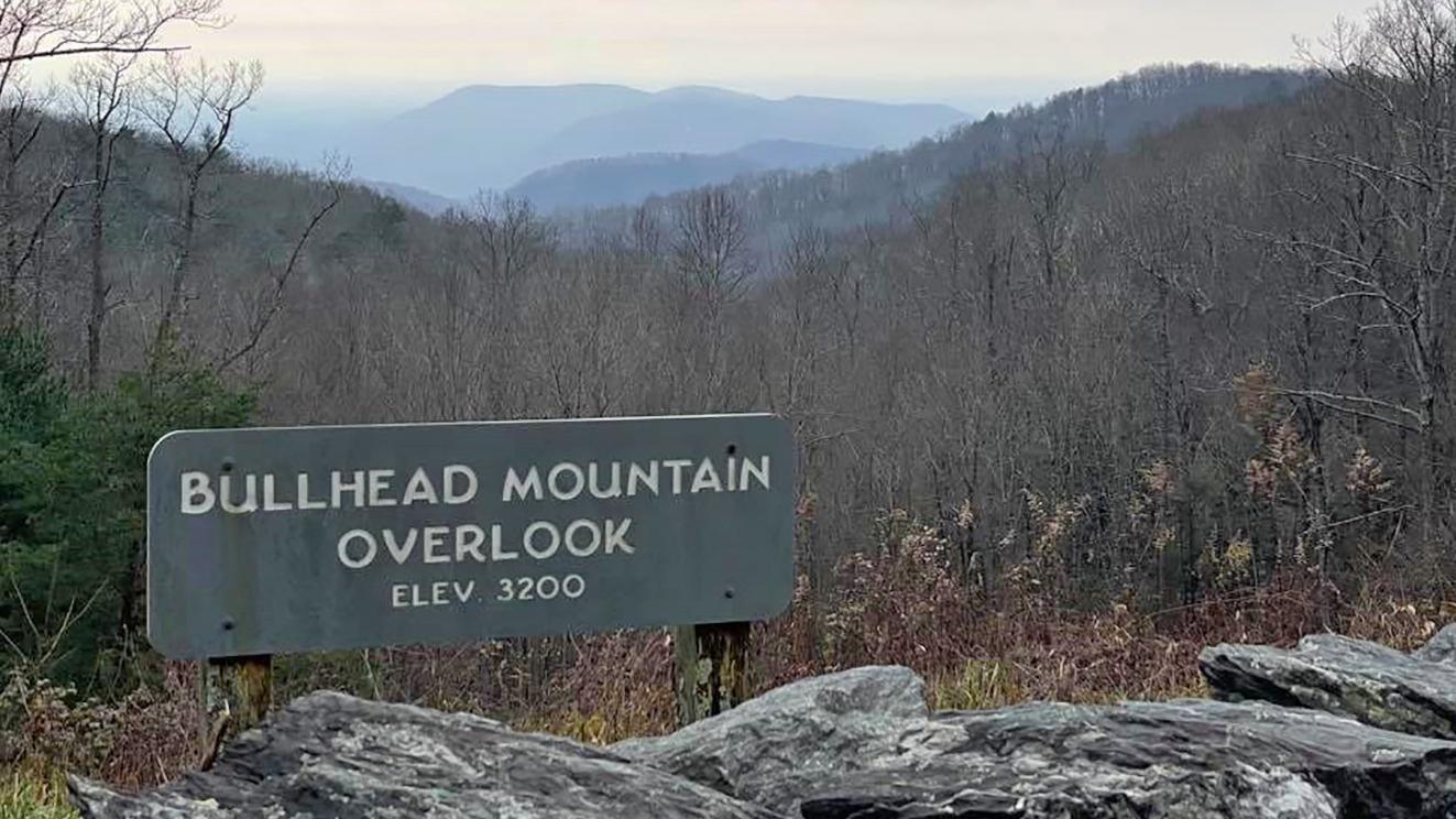 Overlook sign in foreground with bare trees and hazy, distant mountains.