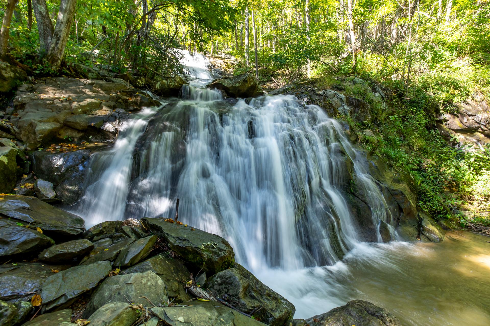 A beautiful waterfall cascades over mossy rocks in a sunlit green forest.