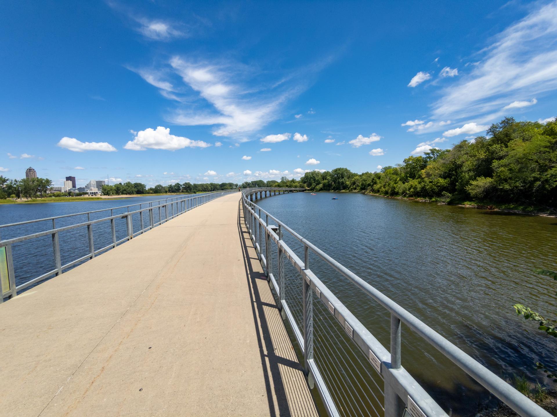 A long paved bridge extends over calm water under a bright blue sky.