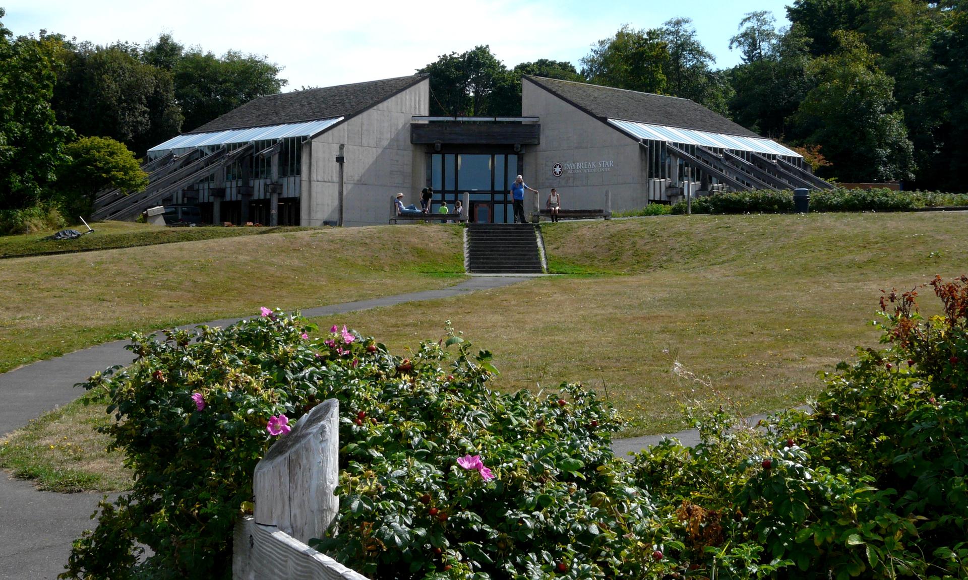 A modern building with a large entrance sits on a grassy hill.