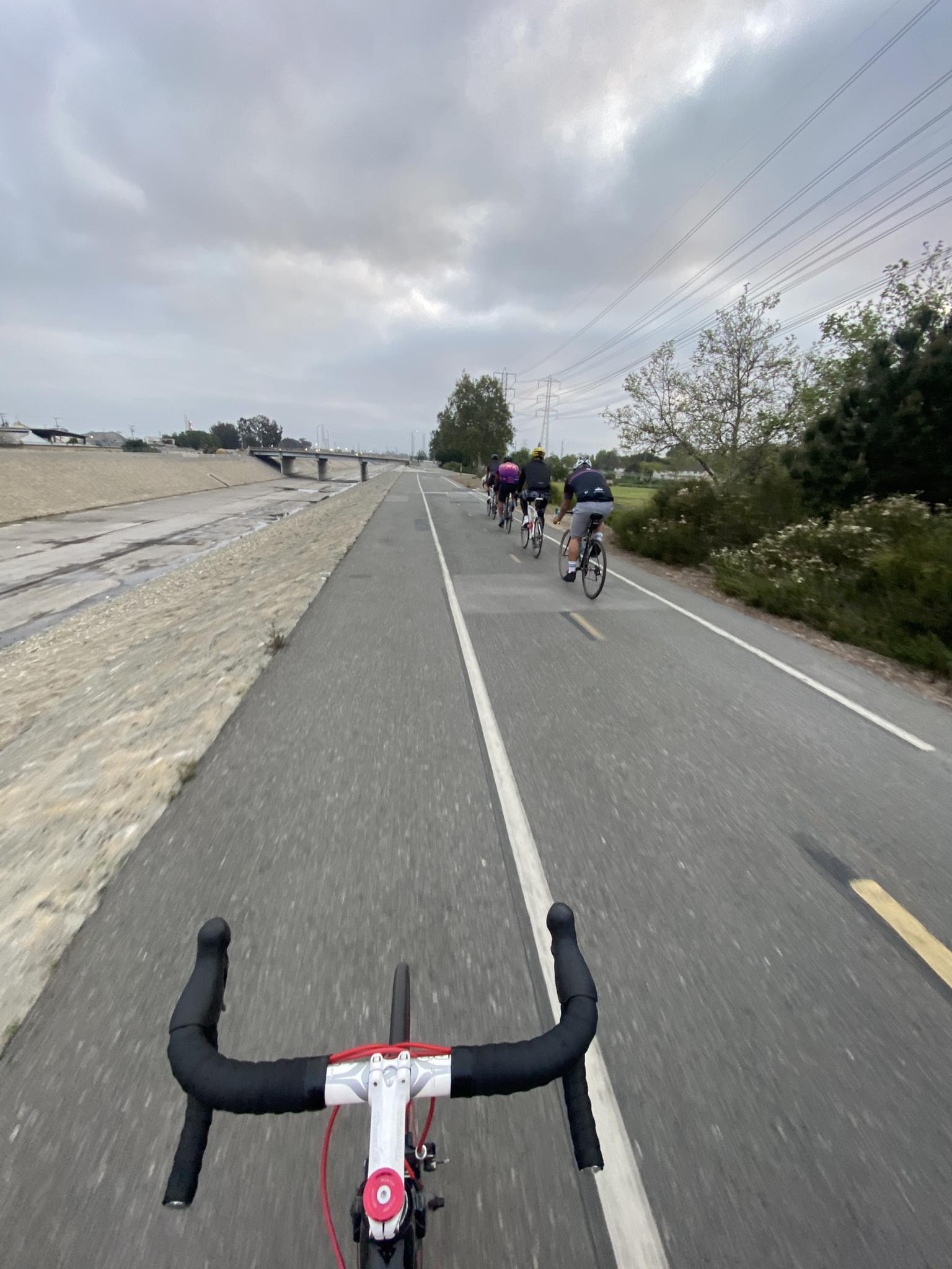Cyclist's view of paved path with group riding under cloudy sky.