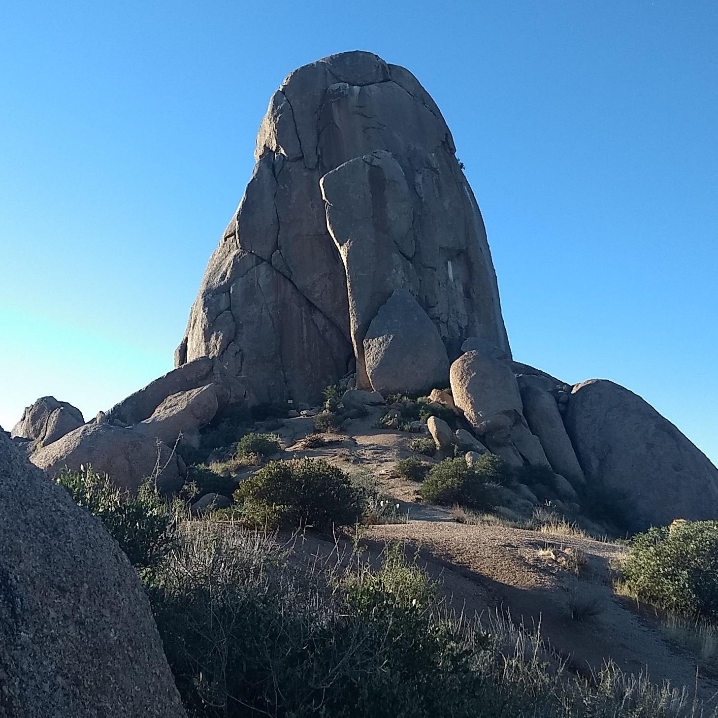 A massive, unique rock formation stands tall under a clear blue sky.