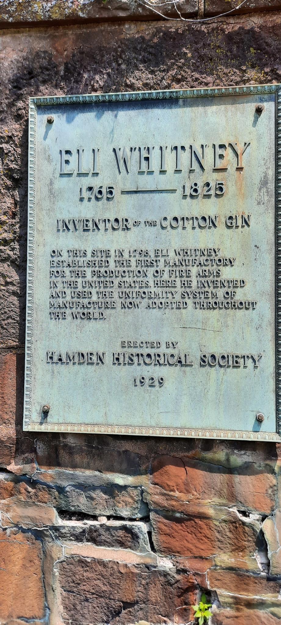 A weathered bronze plaque on a stone wall, detailing historical information.
