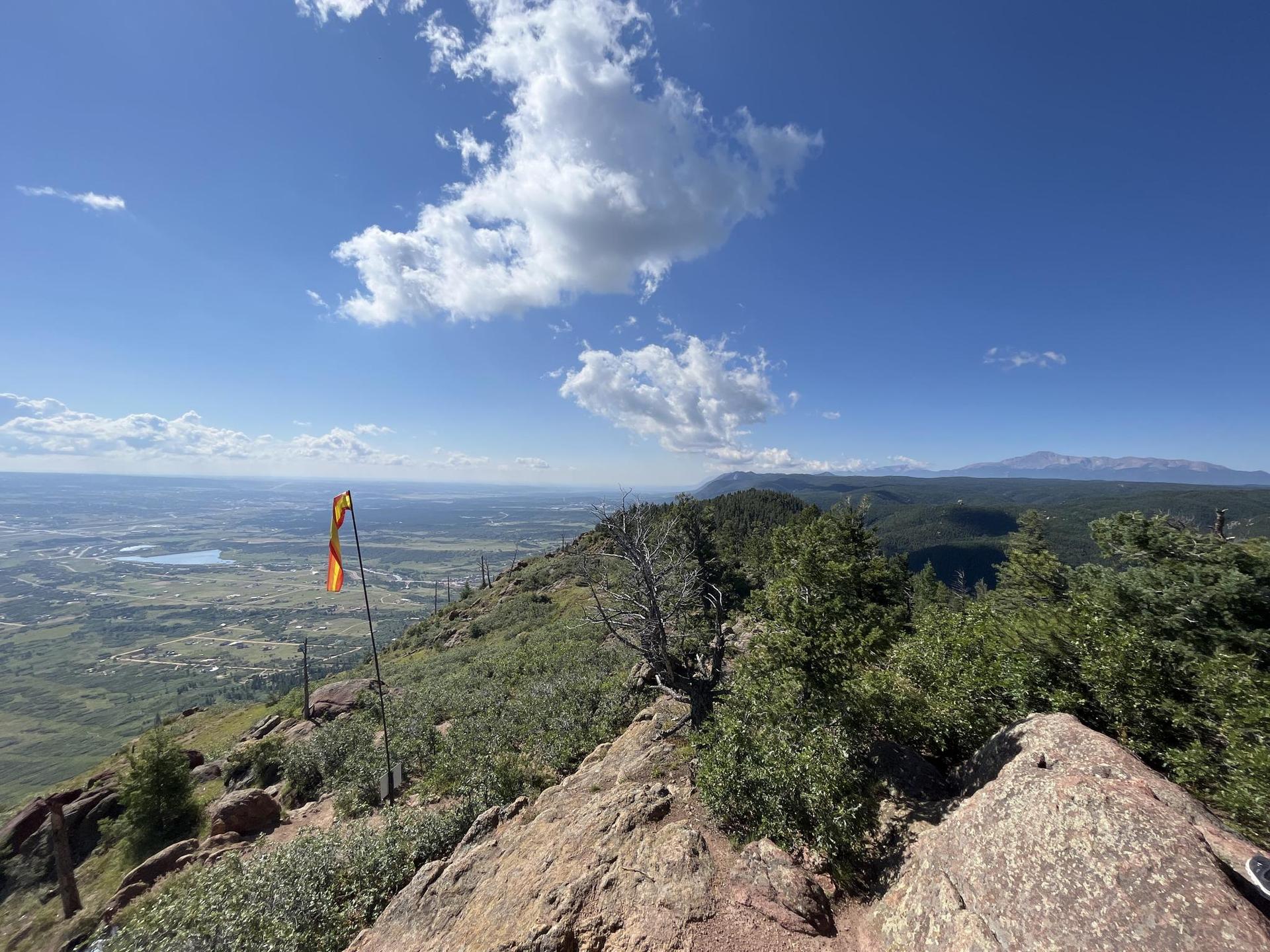 Bright day on a mountain ridge with an orange flag and distant valley.