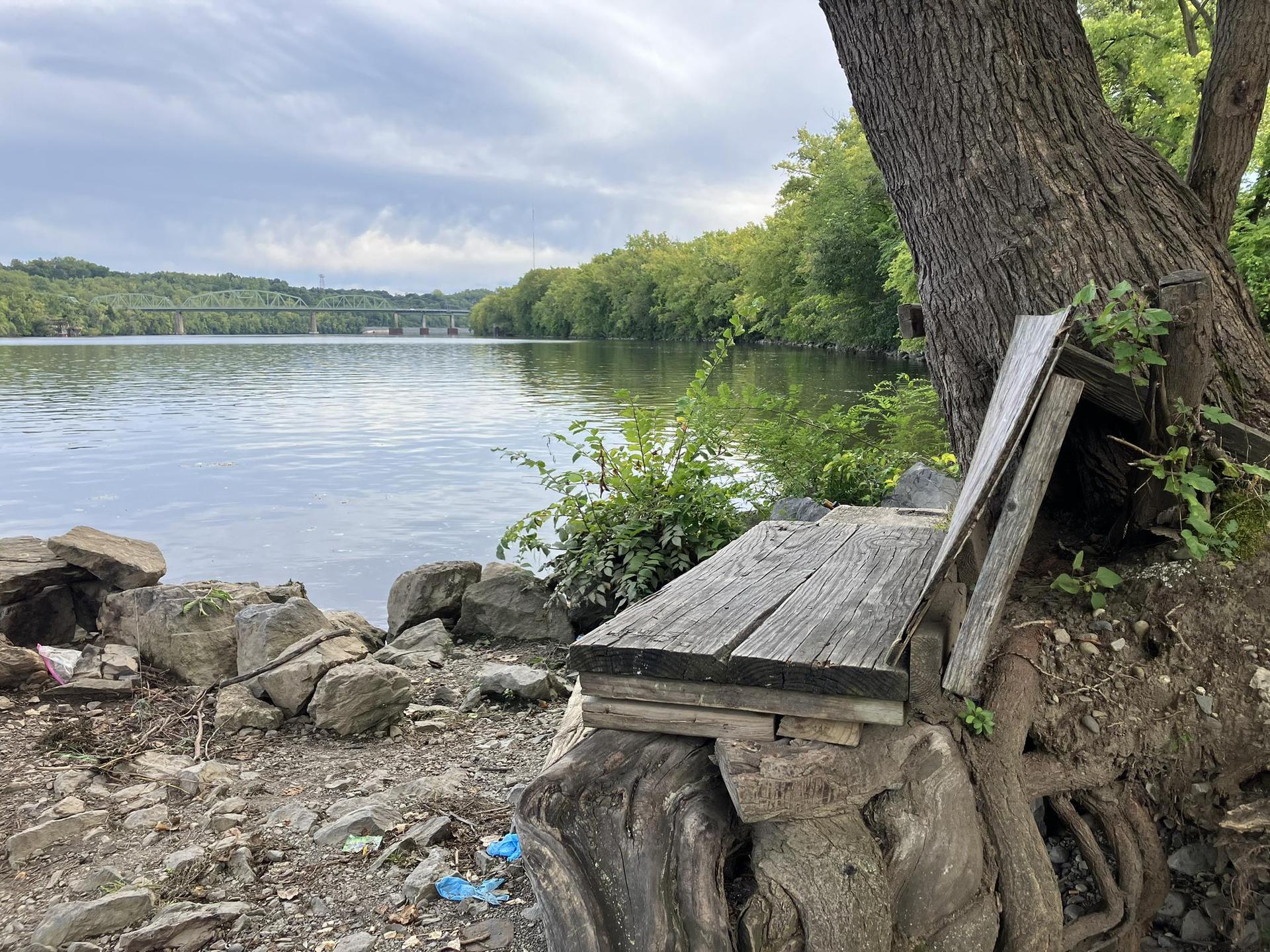 Rustic wooden bench by a rocky riverbank under a cloudy sky.