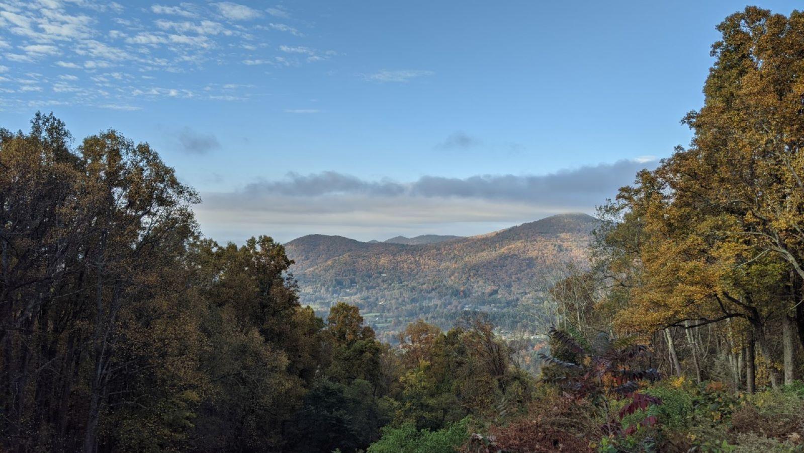 Autumn mountains framed by colorful trees under a partly cloudy sky.
