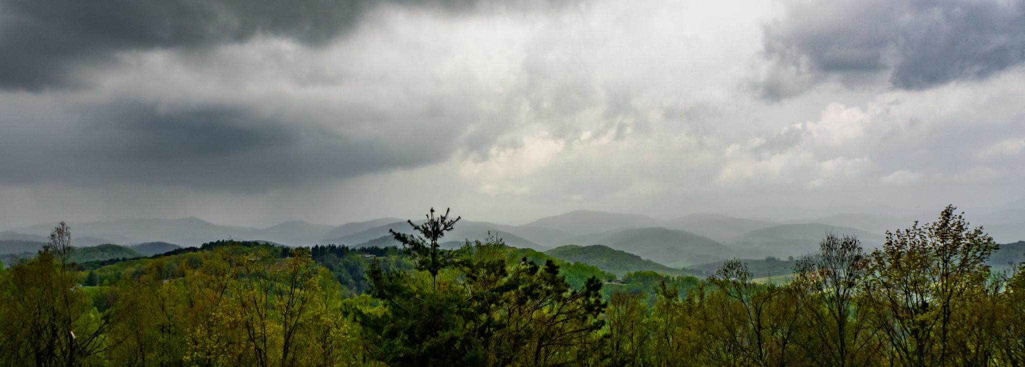 Dark, stormy clouds hang over a vast, forested mountain range.