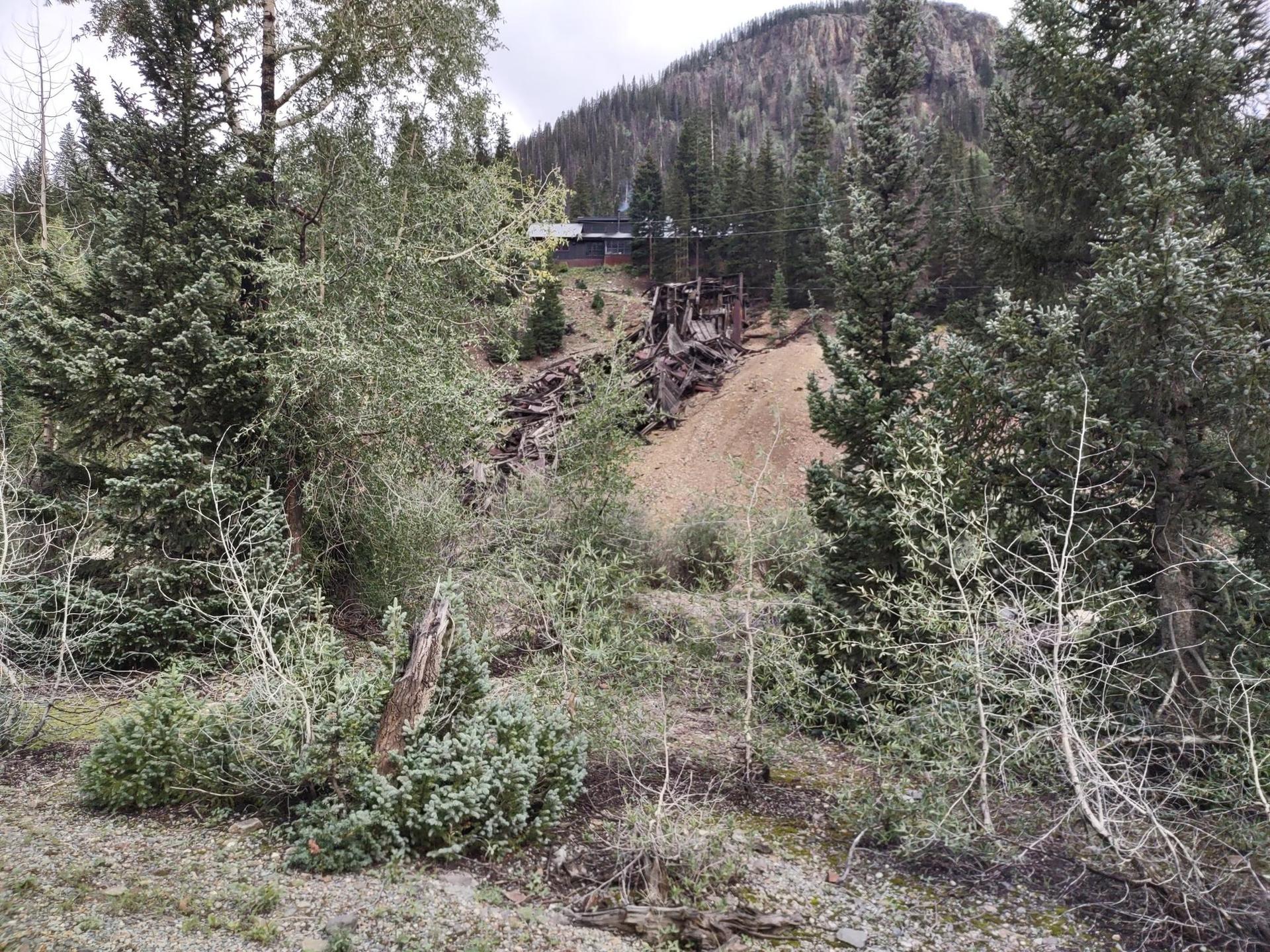 An old mining structure on a forested hillside, surrounded by trees.