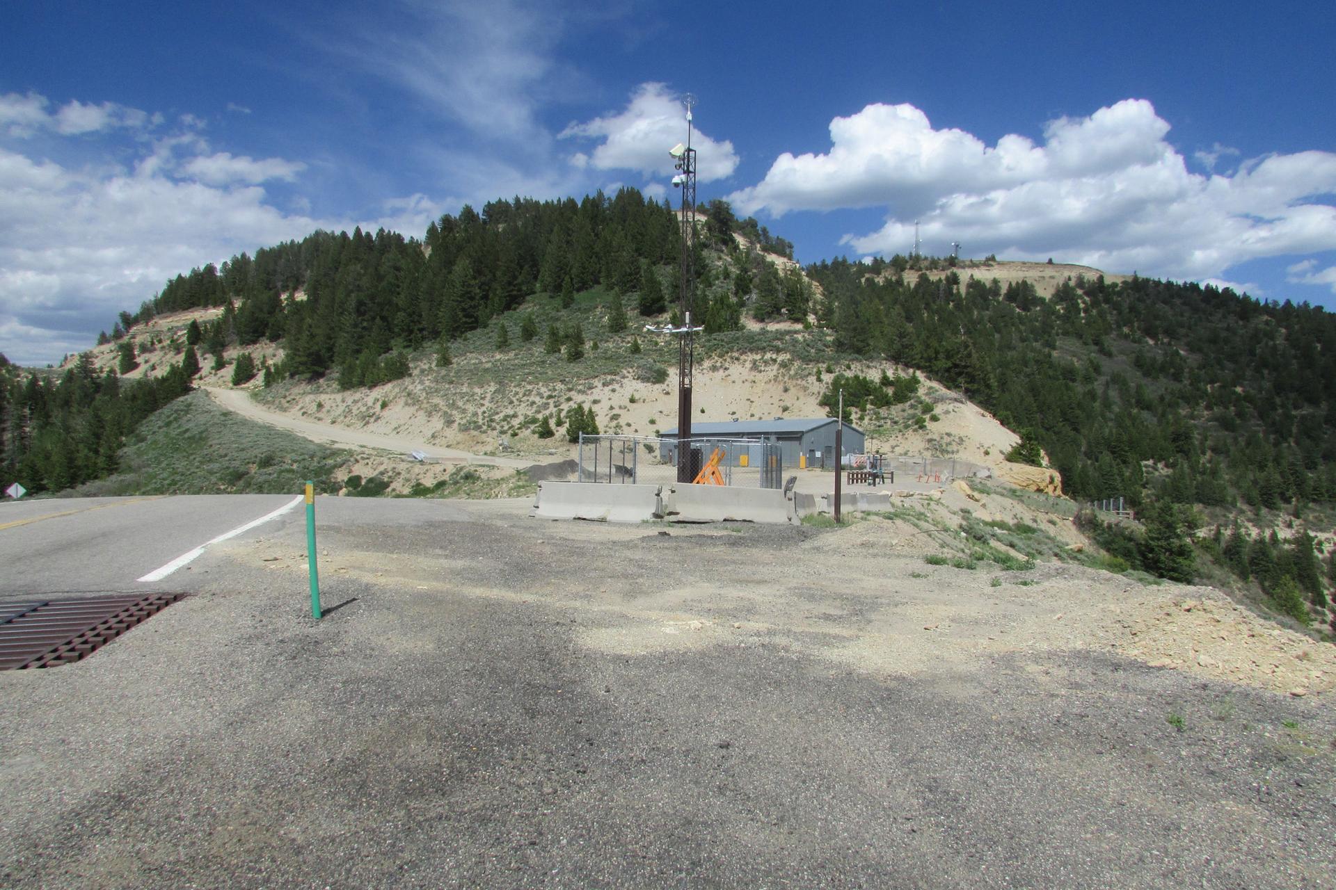 Communication tower and building on a sunny, forested hilltop with a road.
