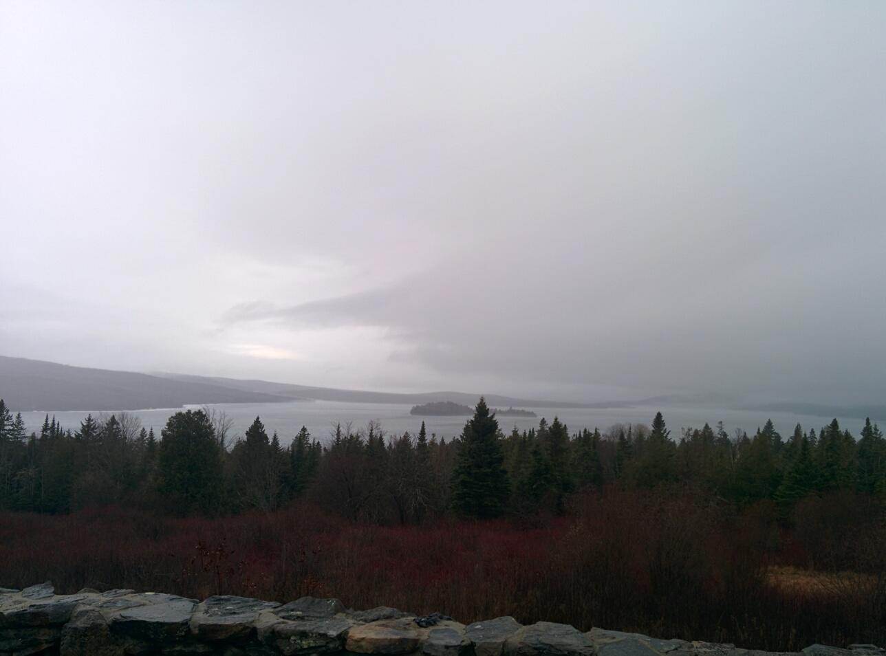 Overcast landscape with a large lake, dense forest, and distant misty mountains.
