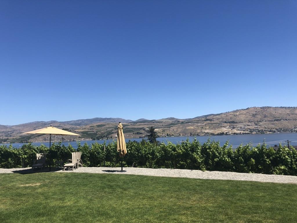 Sunny outdoor patio with umbrellas overlooking a large lake and distant hills.