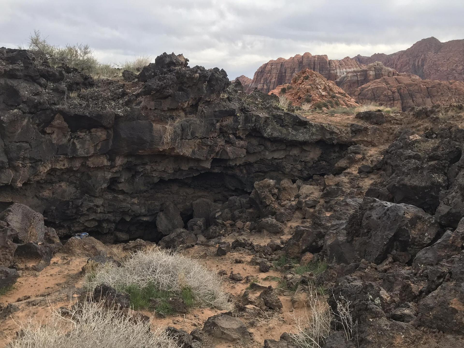 Dark volcanic rock formations with a cave entrance under an overcast sky.